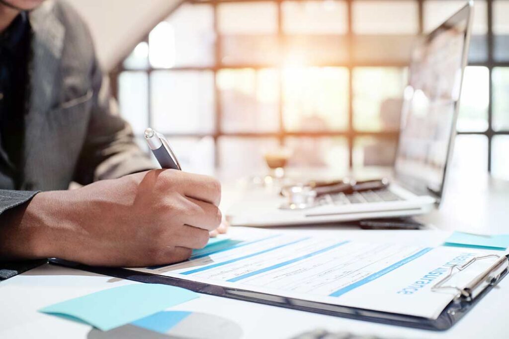Family members review a life insurance policy and funeral documents at a kitchen table.